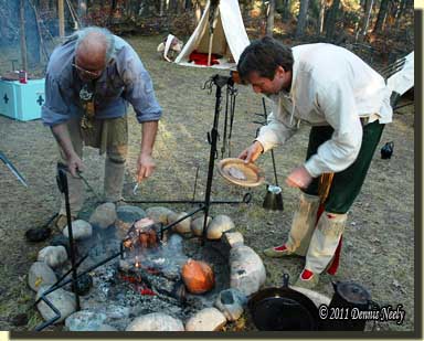 Two traditional hunters slice supper from a venison haunch roasted over an open fire.