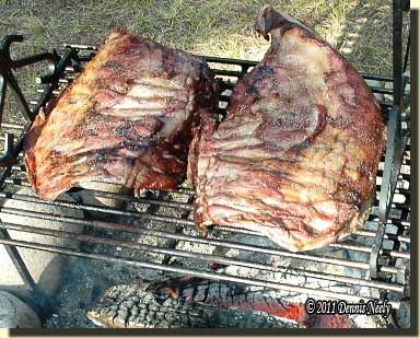 Two racks of venison ribs cooking over red-hot coals.