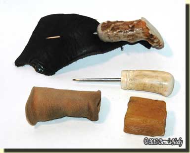 Two antler-handled awls, a leather finger protector and cube of beeswax.