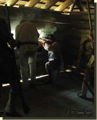 A woodsman fires through the gun port while others load.