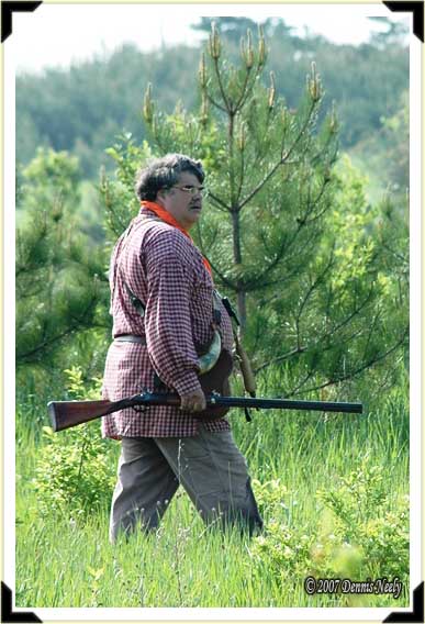 A traditional black powder hunter watches his dog work a pine grove.