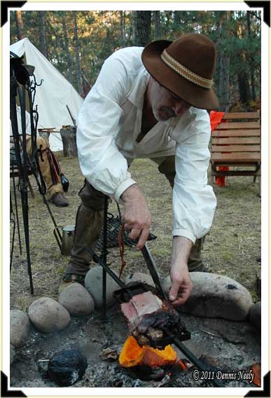 A traditional woodsman slices venison, roasted over an open fire.