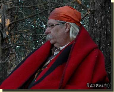 A traditional woodsman sitting wrapped in a trade blanket.