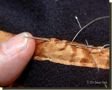 A needle takes two running stitches in the gold ribbon.
