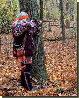 A traditional woodsman taking careful aim from behind an oak tree.