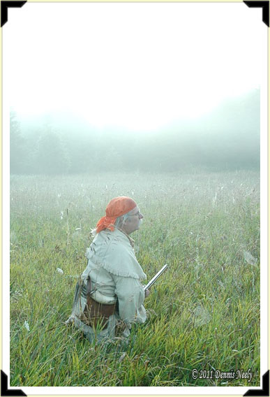 A traditional hunter kneeling in the grass on a foggy morning.