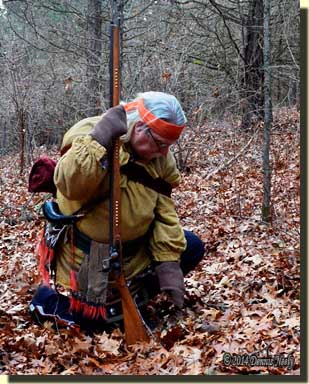 A traditional woodsman brushing leaves from a doe trail.