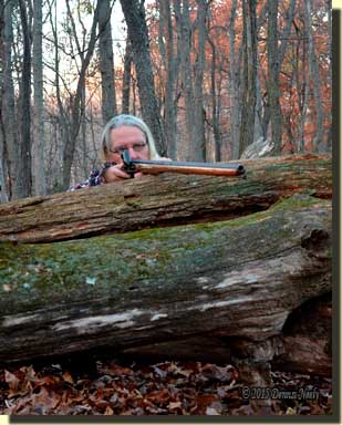 A traditional woodsman rests a Northwest gun over a downed log.
