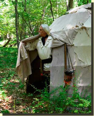 A traditioinal woodsman pushes away the wigwam's flap.