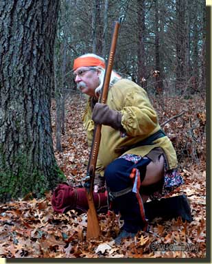 A traditional woodsman dropping to one knee while watching a deer.