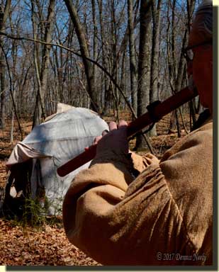 A traditional woodsman playing a Native American flute beside a wigwam.