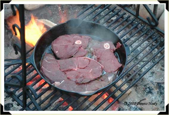 Venison round steak in a cast iron pan over an open fire.
