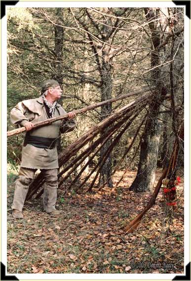 A traditional woodsman adds a pole-rafter to a lean-to shelter.